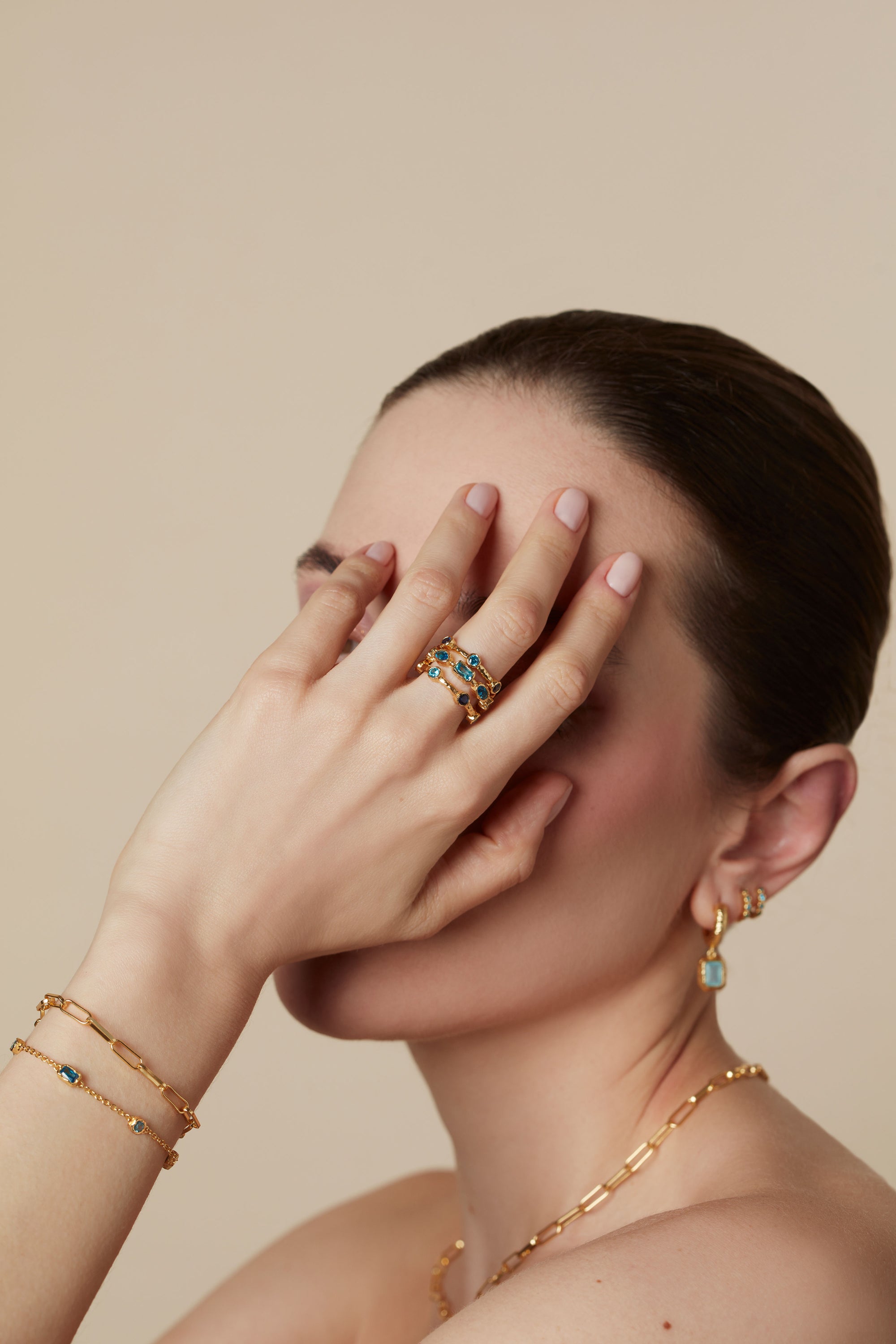 Woman wearing gold jewelry with gemstones on a beige background