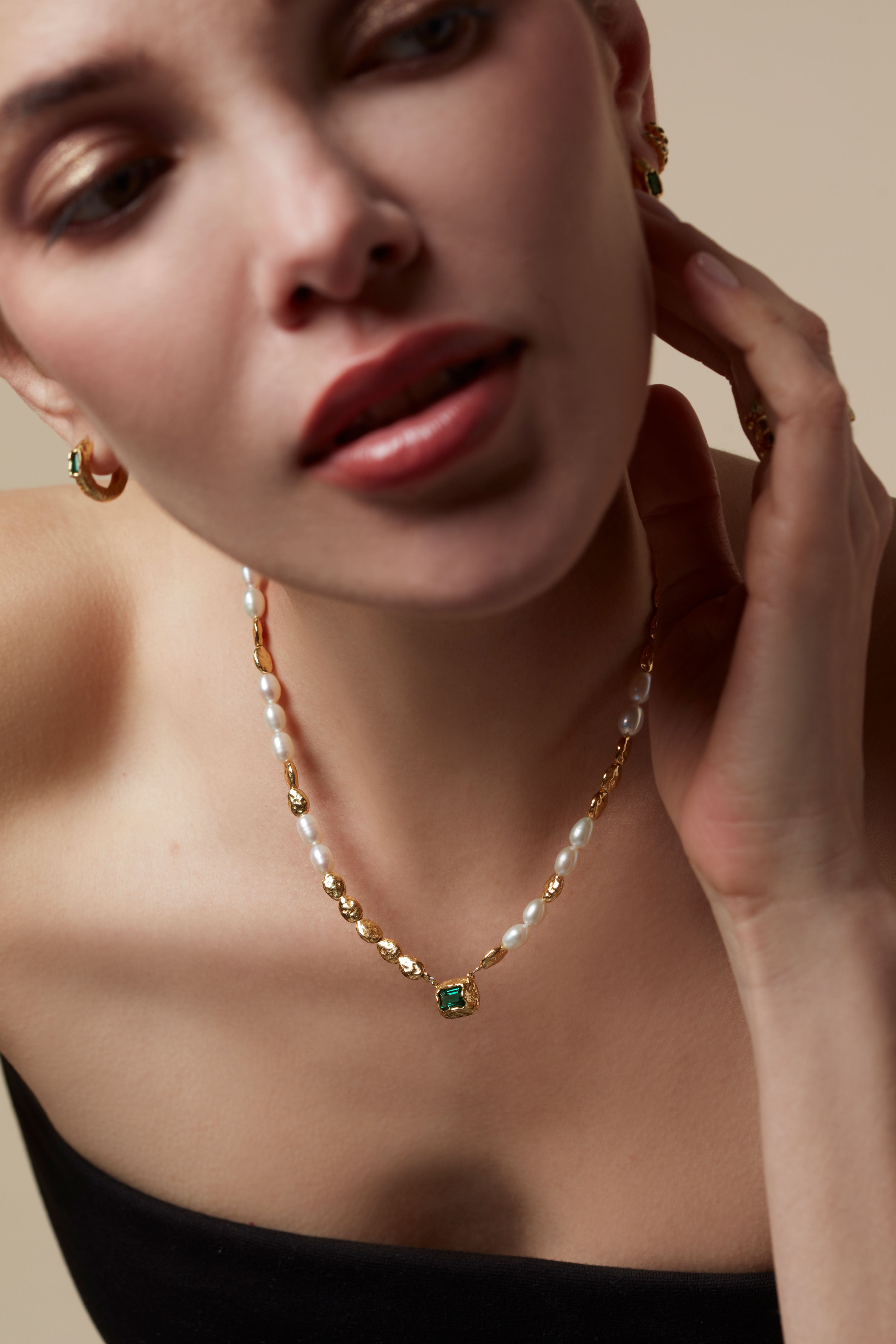 Close-up of a woman wearing a pearl necklace with a green gemstone on a beige background