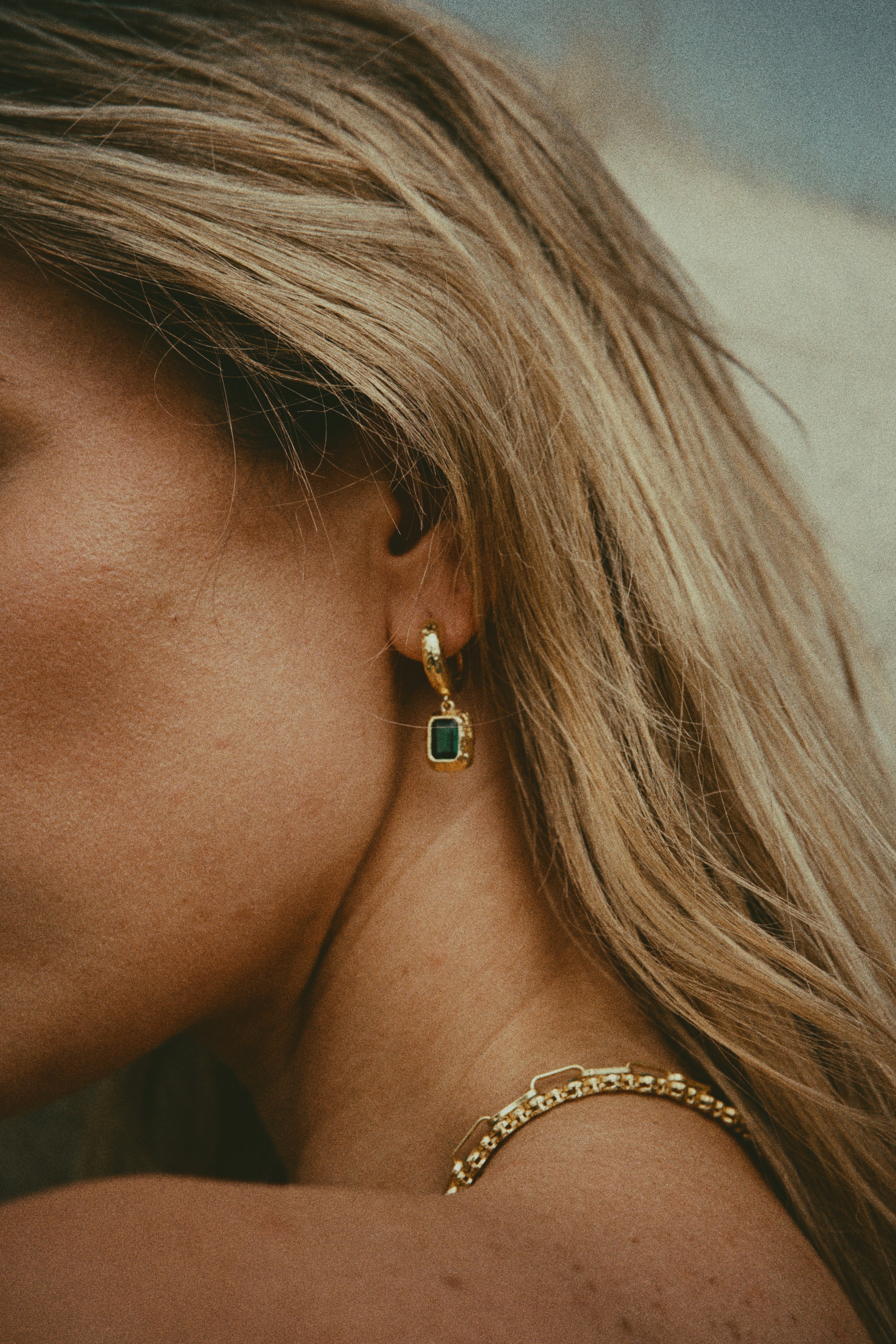 Close-up of a person wearing gold hoop earrings with a green gemstone.